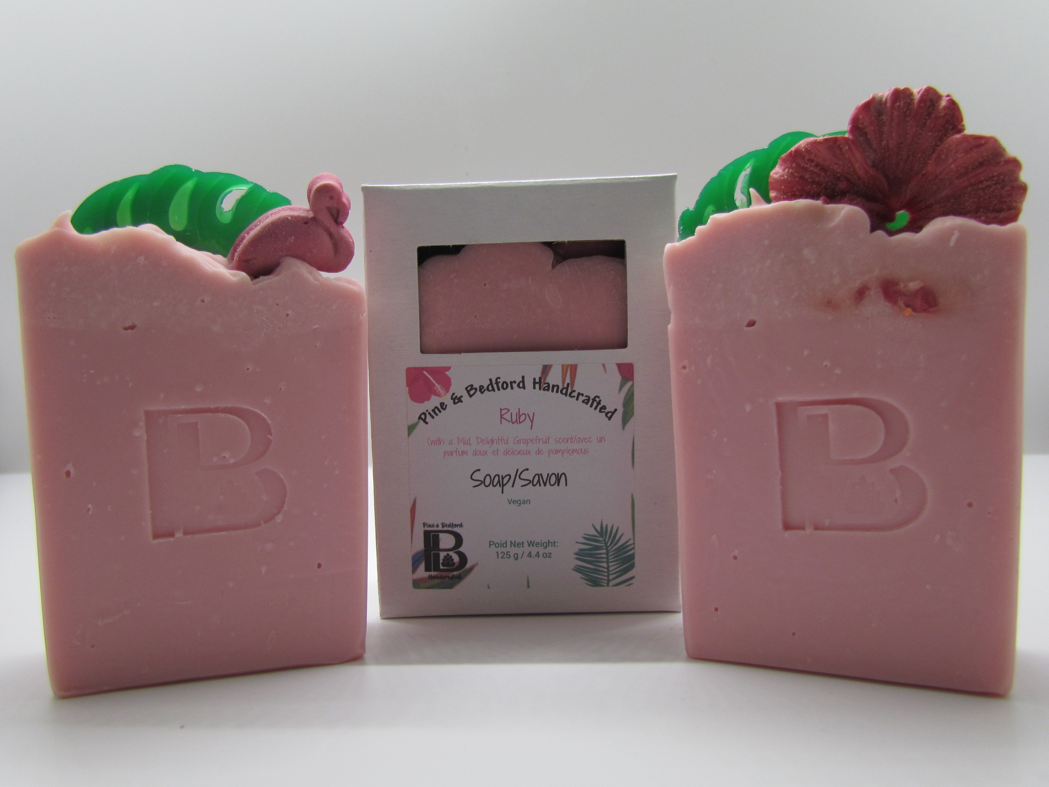 Pine & Bedford's Ruby soap is from our Luxurious Lather Collection. It is lightly fragrance with a fresh-grapefruit fragrance oil.  It is pink with top embellishments of green palm leaves and either a rosy hibiscus or pink flamingo.  Shown naked and boxed.